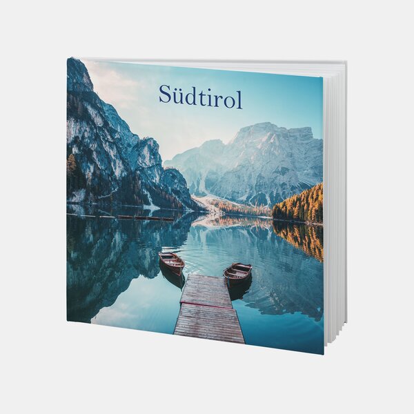 Ein Fotobuch mit dem Titel „Südtirol“ zeigt einen Steg mit zwei Booten vor alpiner Bergkulisse und einem klaren See.
