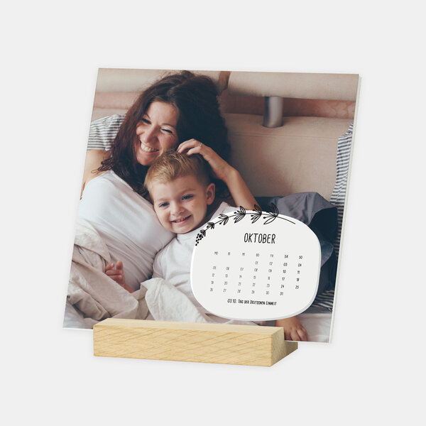 Der Tischkalender im Format 15x15 cm zeigt eine Mutter mit ihrem Kind lachend im Bett, gehalten von einem Holzfuß.
